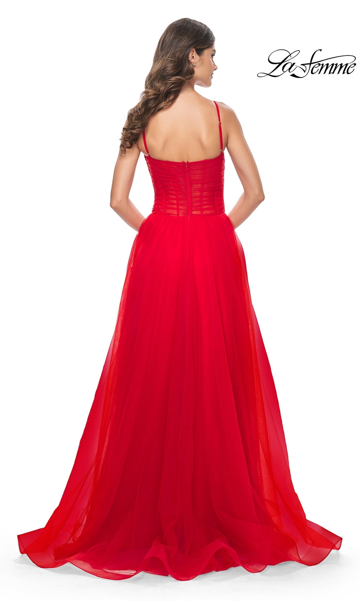 A woman with long brown hair stands with her back to the camera in the La Femme Sheer-Waist Long Prom Ball Gown 32017, featuring thin straps and a sheer overlay. The